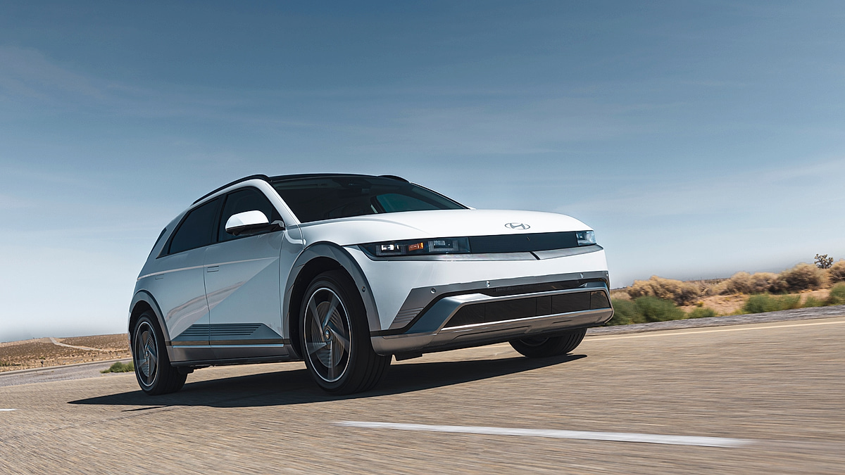 2024 Hyundai Ioniq 5 in Atlas White captured from a dramatic low angle front three quarter perspective while driving on an open desert highway under bright blue skies